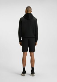 Felpa nera con cappuccio e pantaloni corti abbinati, entrambi realizzati in tessuto liscio. L'outfit presenta una vestibilità comoda e un design minimalista.