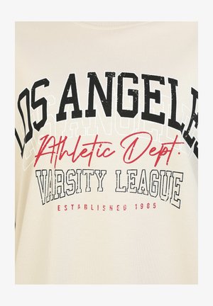 Sweatshirt beige avec un texte noir et rouge en lettres majuscules : "LOS ANGELES," "Département Athletic," "VARSITY LEAGUE," et "ÉTABLI EN 1985." Texture douce.