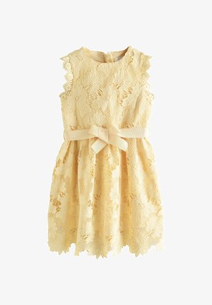 Sárga, ujjatlan csipkeruha virágmintával és hullámos szegélyekkel, deréknál masnira kötött szalaggal.