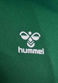 Groene stof met een gladde textuur, met een wit logo van een bij en het woord 'hummel' in vetgedrukte letters.