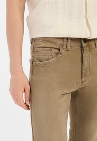 Beige denim jeans met een slim-fit ontwerp, vijf zakken, tonale stiksels en een gladde textuur. De tailleband heeft riemlussen.