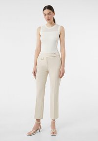 Weißes, geripptes, ärmelloses Top mit einem Mesh-Einsatz, kombiniert mit cremefarbenen, taillierten Hosen mit Seitentaschen und zwei dekorativen Knöpfen.