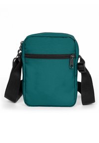 Tearfärgad tygaxelväska med en svart dragkedja och justerbar rem. Har en framficka med dragkedja och rektangulär form. Slät textur.