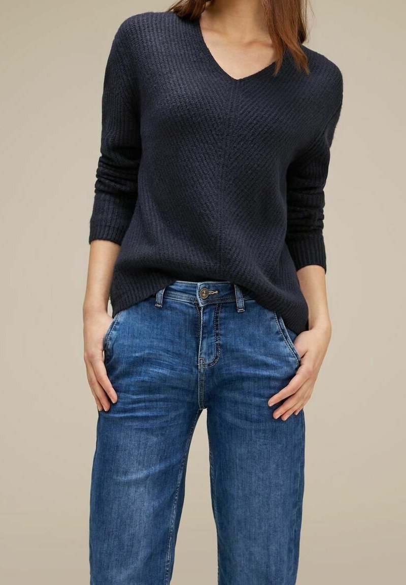 Pull en maille bleu marine avec col en V, manches longues et design texturé, associé à un jean denim bleu clair avec une coupe classique et des poches.