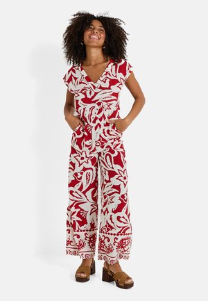 Mono floral rojo y blanco con mangas cortas, escote en V, dos bolsillos laterales y piernas de pantalón acampanadas. Llevado con zapatos de plataforma marrones.