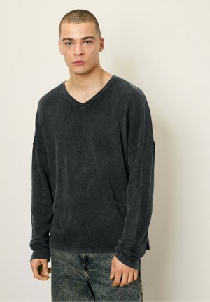 Camisa de cuello en V de manga larga en gris oscuro, hecha de una tela suave, con mangas relajadas y un corte holgado, combinada con unos jeans azules.