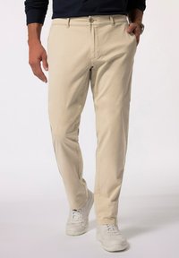 Beige bomullschinos med rak bendesign, knappstängning och framfickor, kombinerat med vita sneakers. Enkel och ren estetik.