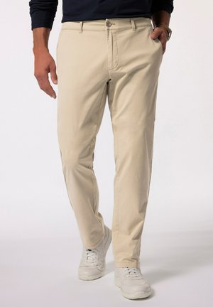Chino in cotone beige con design a gamba dritta, chiusura a bottone e tasche anteriori, abbinati a sneakers bianche. Estetica semplice e pulita.
