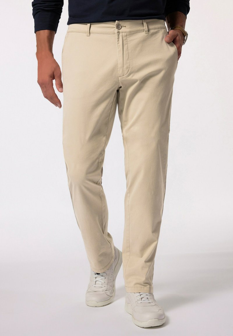 Beige bomullschinos med rak bendesign, knappstängning och framfickor, kombinerat med vita sneakers. Enkel och ren estetik.