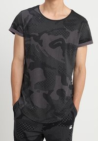 Černé maskáčové tričko s krátkým rukávem a kulatým výstřihem s kontrastním šedým lemem, které je zdobené texturovaným grafickým vzorem po celém povrchu.