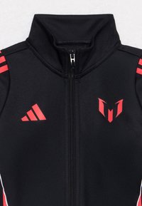 Black zip-up sports jacket with red Adidas logo on the left and red Messi emblem on the right shoulder with red stripes on sleeves.