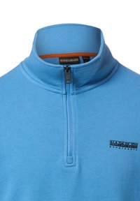 Lichtblauwe trui met rits en opstaande kraag, gemaakt van zacht materiaal, met een hoge hals, een halve rits en een zwart logo aan de linkerkant.