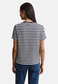 Woman with long dark hair wearing a black and white horizontal striped short-sleeve shirt and blue jeans, viewed from behind.