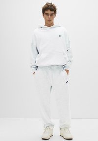 Lichtgrijze hooded sweatshirt en bijpassende sweatpants, gemaakt van zachte stof. Heeft een klein logo op de borst en een elastische tailleband.