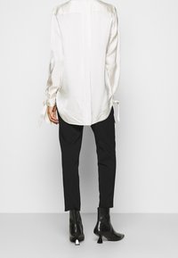 Vit satinblus med långa ärmar och knytaccent, tillsammans med svarta smala byxor och eleganta svarta ankelskor med en metallisk kvadratklack.