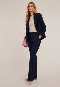Marinblazer och skräddarsydda byxor i kombination med en ribbad beige topp. Accessoarer inkluderar en liten rosa handväska och spetsiga rosa flats.