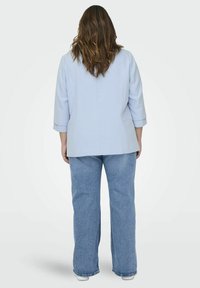 Sinine bleiser kolmandik pikkade varrukatega, koos lõdva siniste teksadega. Materjal tundub siledana ning sellel on struktureeritud disain.