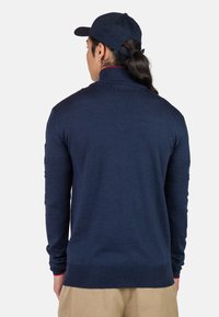 Navyblauer Pullover mit langen Ärmeln und hohem Kragen, mit kontrastierenden roten Akzenten an den Bündchen, aus einem weichen Strickmaterial gefertigt.