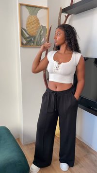 Biały prążkowany crop top z detalem sznurowania, czarne luźne spodnie z kieszeniami i białe sneakersy, na jasnym tle.
