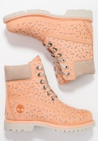 Stivaletti alla caviglia color pesca con motivi ritagliati, dettagli in suede beige, accessori in metallo argentato e suola in gomma bianca.