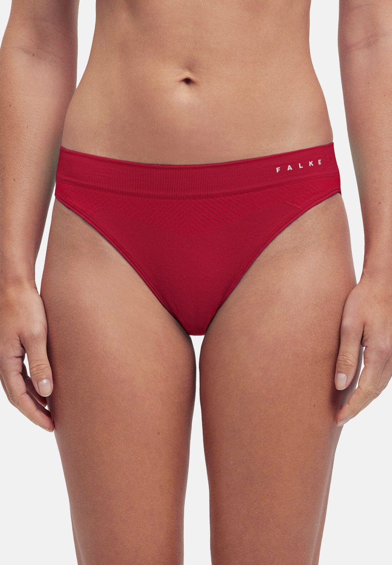 Nahaufnahme einer Frau, die rote nahtlose Slips mit hohem Schnitt und breitem Bund mit dem "FALKE"-Logo an der rechten Hüfte trägt.