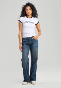 Valkoinen t-paita, jossa on tummansininen reunus ja "NEW YORK" -teksti, yhdistettynä sinisiin farkkuleggingeihin ja valkoisiin tennareihin. Rentoa asukokonaisuutta.