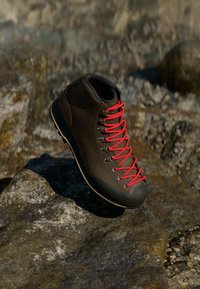 Brune tursko med røde snørebånd, gummikapp på tåen og robust såle på en steinete overflate. Midt-top design med teksturert materiale.