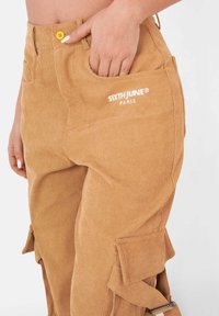 Katoenen cargobroek in een warme bruine kleur met een aansluitende taille, zijzakken, geborduurd logo en verstelbare banden aan de zijkanten.