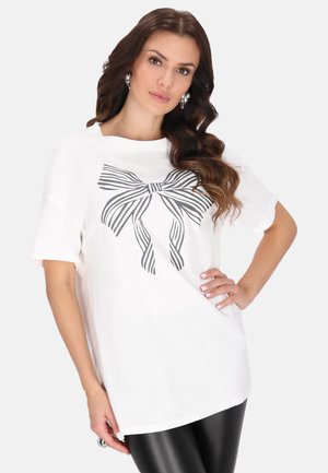 Hvid t-shirt med et sort stribet sløjfeprint på forsiden. Korte ærmer, afslappet pasform og blødt bomuldsstof.