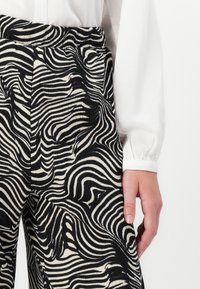 Black and white striped pants with a wavy pattern. Made from textured fabric, featuring a high waist and side pockets.