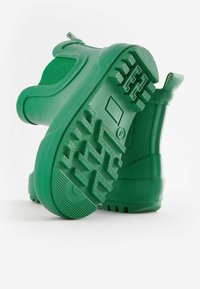Bota de goma verde con suela texturizada, material superior liso y pequeño tacón. El diseño incluye un ajuste ceñido con un bucle trasero para facilitar su uso.