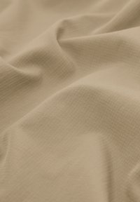 Tissu beige avec un motif en quadrillage subtil, légèrement plié pour montrer la texture et le tombé doux.