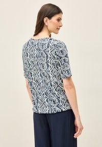 Top a maniche corte in blu navy e bianco, caratterizzato da un motivo geometrico con diamanti e linee, realizzato in tessuto leggero.