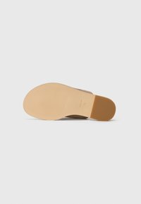 Beige sandaalit korkealla korolla, jossa on teksturoitu pohja ja sileä kumipohja, jossa on vaakasuoria uria pitoa ja vakautta varten.