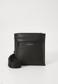 Černá kožená crossbody taška s texturovaným povrchem, nastavitelným popruhem, horním zipem a diskretním logem na přední straně.