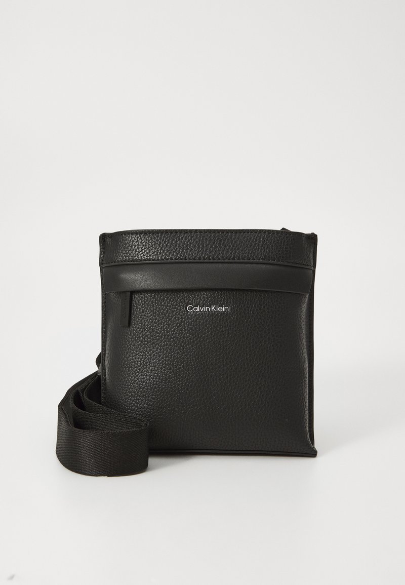 Černá kožená crossbody taška s texturovaným povrchem, nastavitelným popruhem, horním zipem a diskretním logem na přední straně.