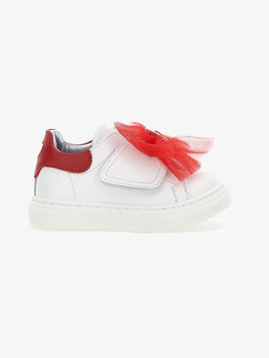 Fehér sneaker piros díszítéssel és tüll masnival. Velcro záródás és strukturált fehér gumitalp jellemzi. Simas bőr anyag.