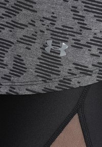 Nära bild av grått mönstrat tyg med Under Armour-logotyp ovanför svart mesh i sömmen av ett atletiskt plagg.