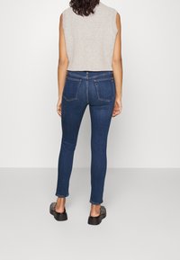 Tajta, mörkblå jeans av denim med bakfickor och minimala sömdetaljer, tillsammans med en ljusgrå ärmlös topp och svarta skor.