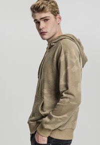 Beige camo hettegenser med frontlomme, justerbar snorhette og ribbede mansjetter. Myk tekstur med en avslappet passform.