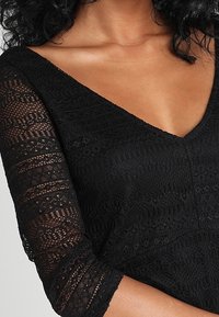 Black lace dress featuring a V-neck, three-quarter sleeves, and textured pattern throughout the fabric, showcasing intricate detailing.