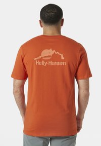 Oranžové bavlněné tričko s grafikou hory a slunečním designem ve světle oranžové, s textem "Helly-Hansen" na zadní straně. Krátké rukávy.
