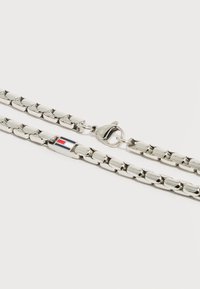 Ασημένιο κολιέ με αλυσίδα από ορθογώνιους κρίκους, με κούμπωμα καβουράκι και ένα μικρό ορθογώνιο φυλαχτό με κόκκινες, λευκές και μπλε ρίγες.