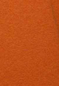 Acercamiento a una tela suave con una superficie texturizada de color naranja que muestra sutiles variaciones en el color y el patrón de tejido.