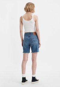 Shorts en jean avec un ourlet effiloché, couleur bleu clair, design à cinq poches, patch en cuir au dos, associés à un débardeur blanc et des baskets montantes noires.