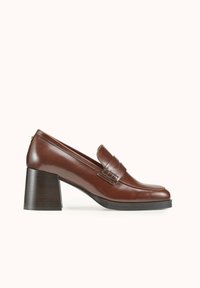 Mocassins à talons en cuir marron avec un bout arrondi, une sangle décorative et un talon bloc texturé. Fini lisse et détails de couture subtils.