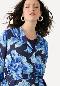 Bloemige shirt in blauwe en marine stof, met een kraag, knoopdetails met een kleine versiering en een gestrikt tailleband.
