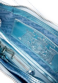 Intérieur d'un sac à main zippé bleu clair présentant une finition texturée brillante, un détail de logo embossé et un doublure à motifs.