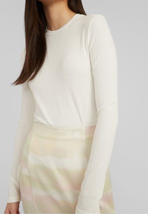 Femme portant un haut à manches longues côtelé blanc et une jupe pastel aux nuances douces de rose et de vert.