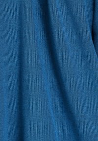 Gestructureerde blauwe gaasstof met een hexagonaal patroon dat diepte uitstraalt, en dat een ademend en lichtgewicht ontwerp toont.